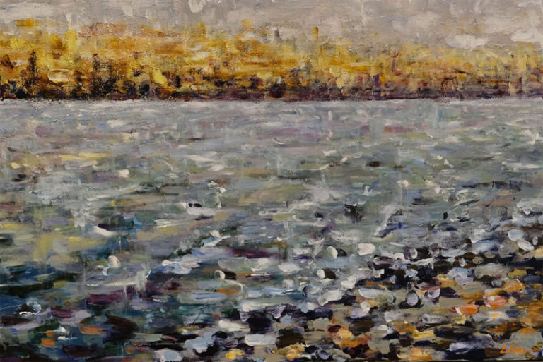 Multicoloured river water with distant golden trees seen from the water’s edge amid dark rocks.